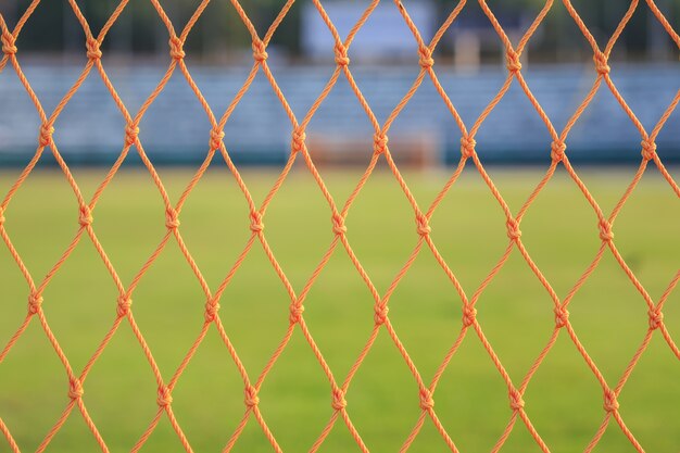 Schließen Sie herauf orange Fußballnetz auf Hintergrund des grünen Grases