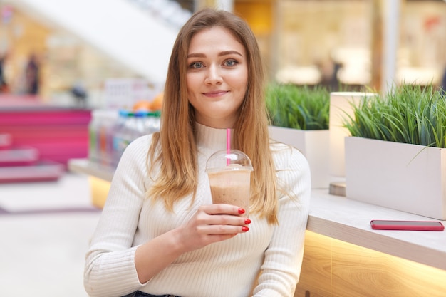 Schließen Sie herauf Porträt der attraktiven blonden Frau, die am Morgen im Restaurant Limonade trinkt, lässiges weißes Hemd tragend, hat langes blondes Haar, schaut lächelnd direkt in Kamera.