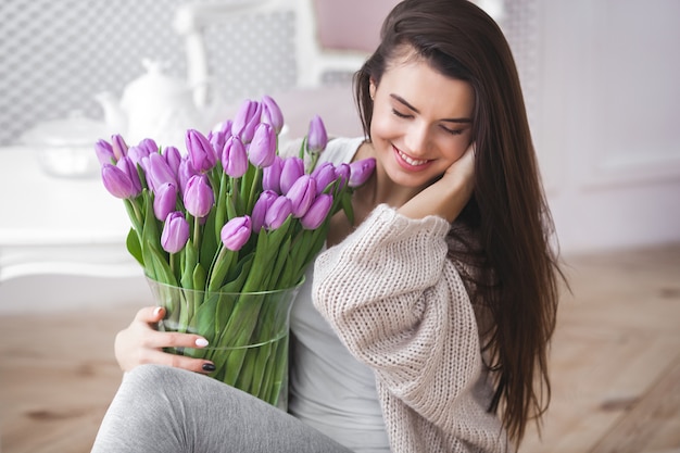 Schließen Sie herauf Porträt der schönen jungen Frau, die Blumen hält. Attraktive Frau mit Tulpen