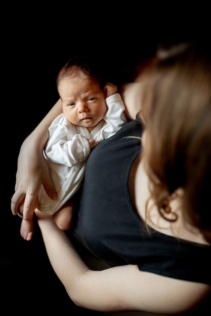 Schließen Sie herauf Porträt der schönen jungen Mutter mit neugeborenem Baby auf schwarzem Hintergrund, Kopienraum