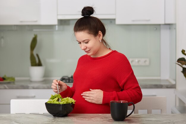 Schließen Sie herauf Porträt der schwangeren Frau, die frischen grünen Salat in der Küche kocht