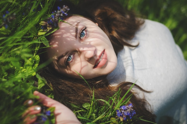 Schließen Sie herauf Porträt des jungen lächelnden Mädchens mit den blauen Augen, die auf Gras im Garten liegen.