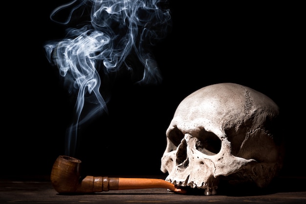 Schließen Sie herauf Porträt des menschlichen Schädels mit Rauchpfeife und Rauch auf schwarzem Hintergrund