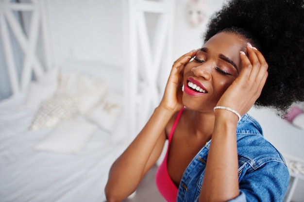 Schließen Sie herauf Porträt einer attraktiven Afroamerikanerfrau mit Afro-Haar tragen Jeansjacke, gestellt am weißen Raum. Modisches schwarzes Modell.