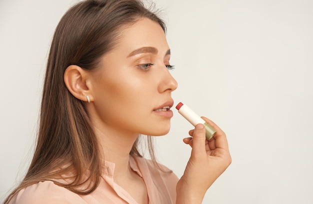 Schließen Sie herauf Porträt einer ernsten zufriedenen Frau, die roten Lippenbalsam anwendet Seitenansicht Studioaufnahme über grauem Hintergrund