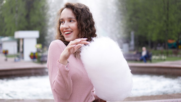 Schließen Sie herauf Porträt einer glücklichen lächelnden aufgeregten Frau, die Zuckerwatte am Vergnügungspark hält