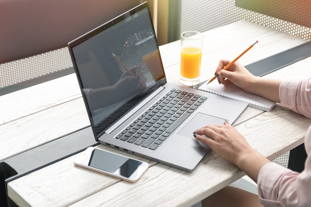 Schließen Sie herauf Porträt einer jungen Frau, die auf dem Tisch an Laptop arbeitet und, Orangensaft schreibt.