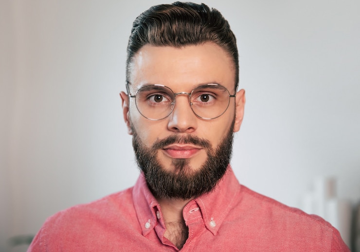 Foto schließen sie herauf porträt eines attraktiven, eleganten und selbstbewussten bärtigen mannes in brille und hemd zu hause, während er in die kamera schaut
