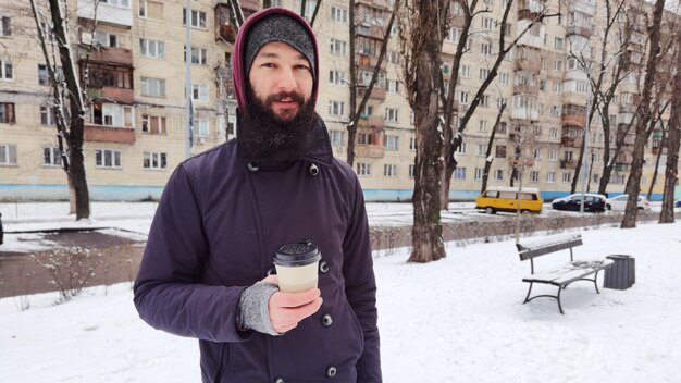 Schließen Sie herauf Porträt eines bärtigen jungen Mannes, der Kaffee zum Mitnehmen trinkt