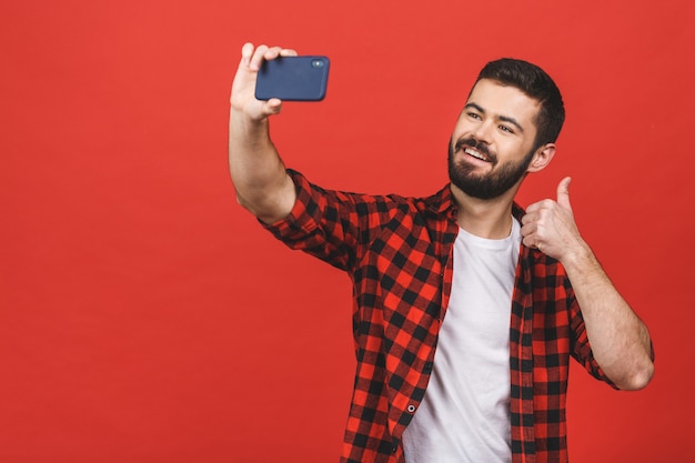 Schließen Sie herauf Porträt eines fröhlichen bärtigen Mannes, der selfie über rote Wand nimmt. Daumen hoch.
