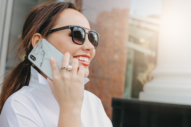 Schließen Sie herauf Porträt von Geschäftsdame eleganter Frau des Brunette in der Sonnenbrille unter Verwendung des Mobiles