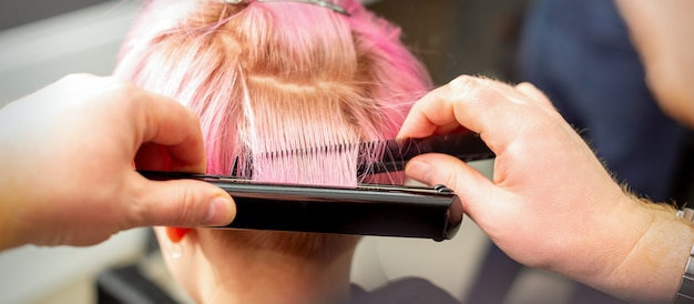 Foto schließen sie herauf rückansicht der hände des friseurs, die kurzes rosa haar mit einem haarbügeleisen glätten