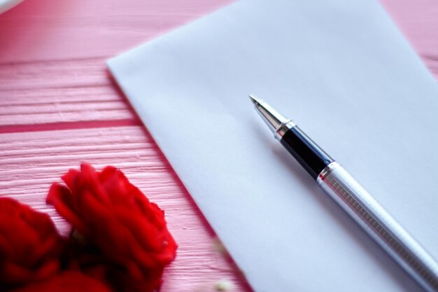 Schließen Sie herauf Stift auf weißem leerem Papier und roten Blumen