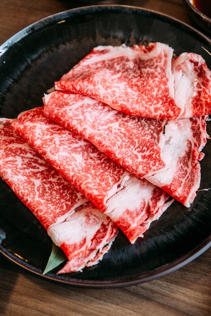 Schließen Sie herauf Sukiyaki-Satz einschließlich seltene Scheiben Wagyu A5 Rindfleisch mit hoch-marmorierter Beschaffenheit im schwarzen Teller.