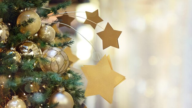 Schließen Sie herauf Weihnachtsbaum verziert mit goldenen Kugeln und Sternenkugel auf Girlande Licht Bokeh Hintergrund für Grußkarte mit Platz für Text