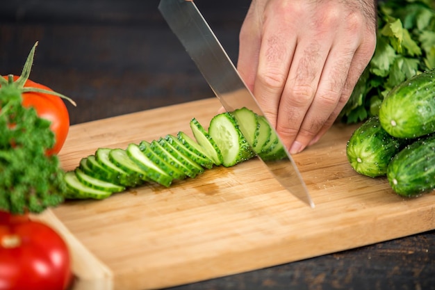 Schließen Sie oben auf den männlichen Händen, die Gurke schneiden und Salat machen. Chef schneidet Gemüse. Gesunder Lebensstil, Diätkost