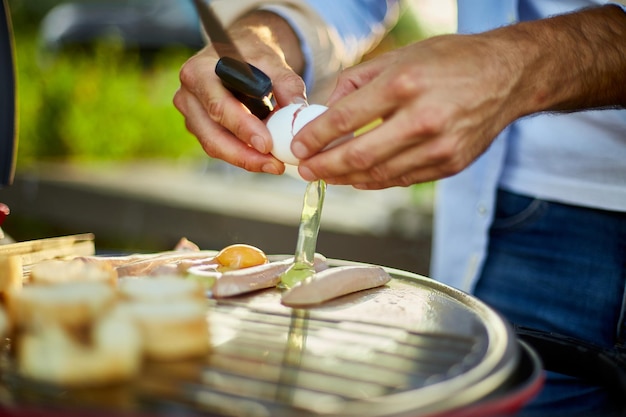 Schließen Sie oben auf der Hand des Mannes, Eier zu brechen, die Bruschetta und Würstchen braten