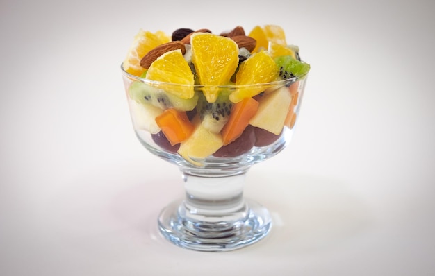 Schließen Sie oben auf einer Glasschüssel, die mit einem frischen und bunten Fruchtsalat gefüllt wird Orange Frucht Kiwi Papaya Melone Apfel Mandel