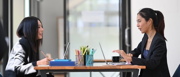 Schließen Sie oben auf zwei freundliche Geschäftsfrauen, die zusammen am Projekt im modernen Büro arbeiten