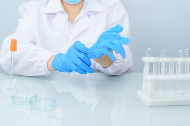 Schließen Sie oben die Hände des Wissenschaftlers, die nitrilblaue Latexhandschuhe im Laborkittel mit Nitrilhandschuhen anziehen und Experimente im Labor durchführen