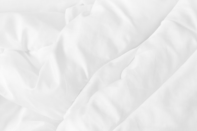 Schließen Sie oben Draufsicht des weißen Bettlakenes und der faltigen unordentlichen Decke im Schlafzimmer nach dem Aufwachen am Morgen.