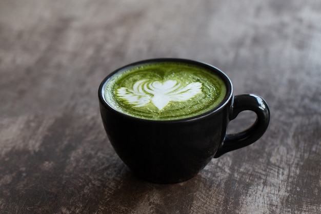 Schließen Sie oben eine Tasse Matcha grüner Tee spätes Kunstheißgetränk auf hölzernem Tischhintergrund