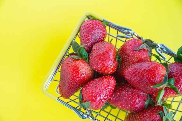 Schließen Sie oben frische Erdbeeren mit einem Einkaufskorb auf einem hellen gelben Hintergrund. Werbekonzept für frische Produkte. Speicherplatz kopieren