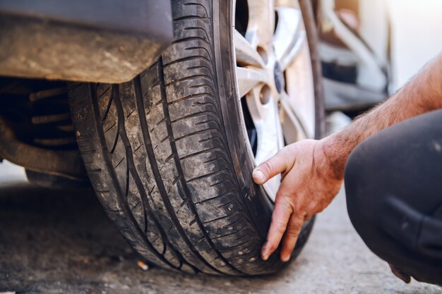 Schließen Sie oben vom Automechaniker, der Reifen während des Hockens in der Werkstatt wechselt.