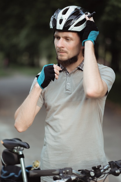 Schließen Sie oben vom bärtigen Lieferboten, der Helm trägt, während Sie mit Fahrrad draußen stehen, bereit, ein Fahrrad zu fahren