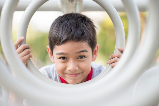 Schließen Sie oben vom Gesicht des kleinen Jungen, das an der Zyklusstange am Spielplatz hängt