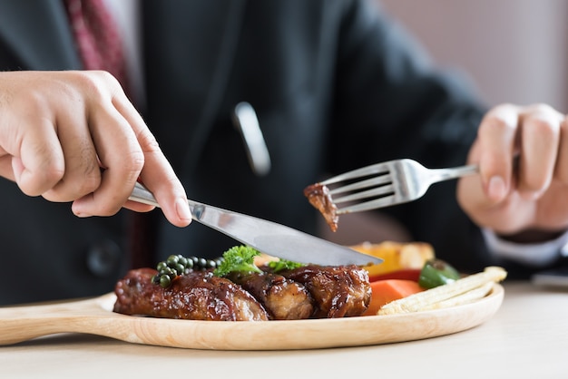 Schließen Sie oben vom jungen Geschäftsmann, der Rippensteak auf hölzernem Behälter am Restaurant isst.