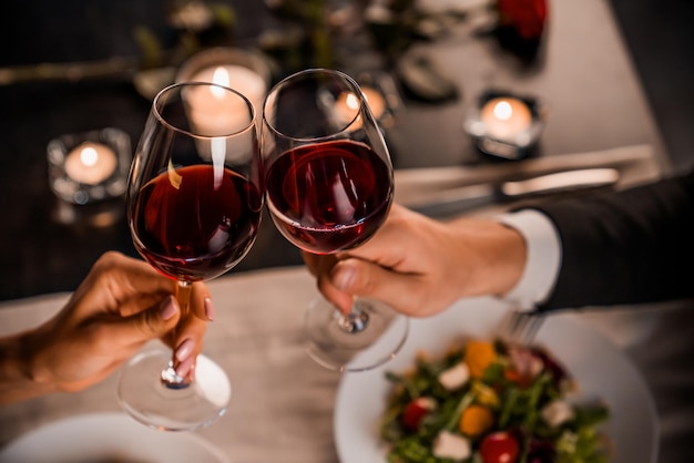 Schließen Sie oben vom jungen Paar, das mit Gläsern Rotwein am Restaurant röstet