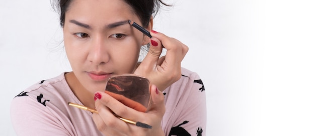 Schließen Sie oben vom schönen Gesicht der jungen asiatischen Frau, die Make-up erhält. Die Künstlerin trägt mit Pinsel und Bleistift Lidschatten auf ihre Augenbrauen auf. Dame schloss die Augen vor Entspannung