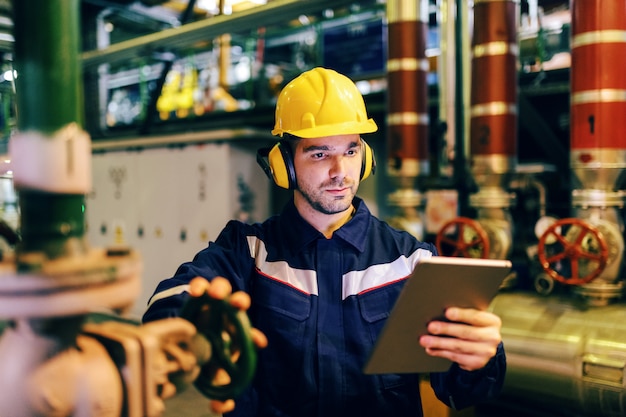 Schließen Sie oben vom Schutzanzug des Arbeiters, während Sie Tablette verwenden und das Ventil festziehen, während Sie im Heizwerk stehen.