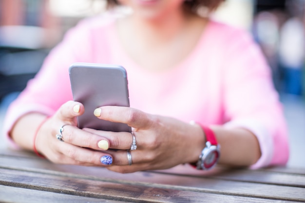 Schließen Sie oben vom Smartphone der hinteren Ansicht in den Frau manikürten Händen auf Holztisch.