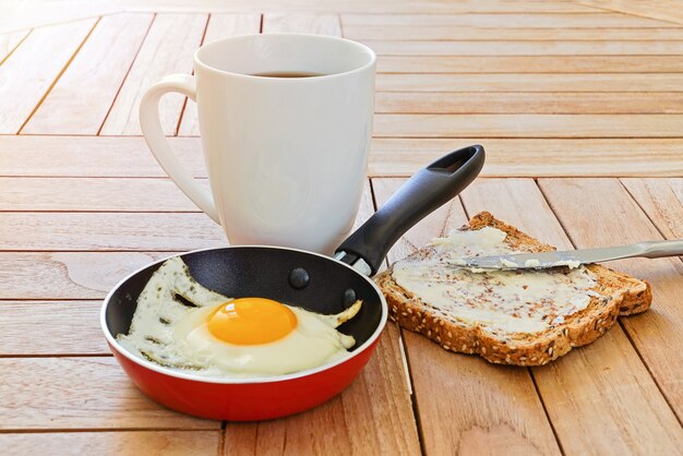 Schließen Sie oben vom Spiegelei im Topf, im Toast und im Becher Kaffee auf Holztisch