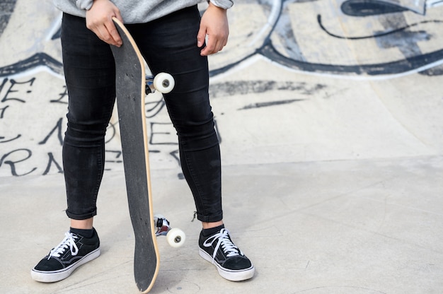 Schließen Sie oben vom unerkennbaren jungen Mann, der Longboard oder Skateboard im Park hält.