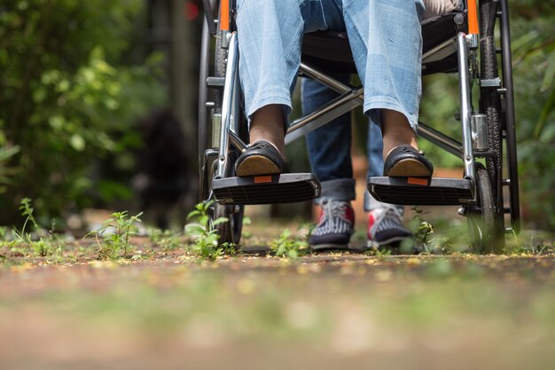 Schließen Sie oben von den Füßen der älteren Frau im Rollstuhl, der mit der Pflegekraft geht