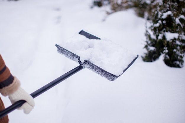 Foto schließen sie oben von den händen der jungen frau, die schnee vom weg schaufeln