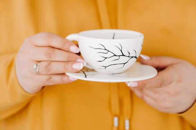 Schließen Sie oben von den Händen einer Frau in einem orange Sweatshirt, das eine Kaffeetasse hält.