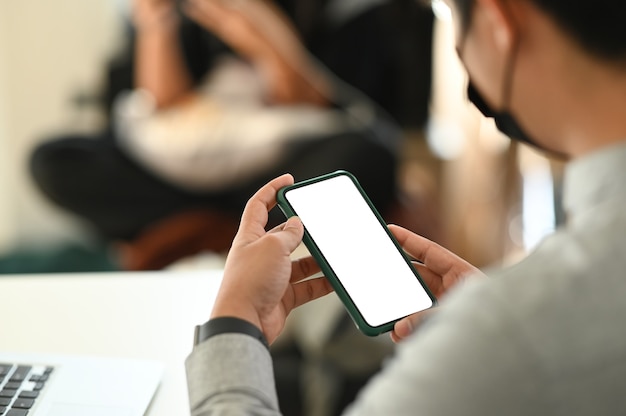 Schließen Sie oben von den Mannhänden, die verspotteten leeren Smartphonebildschirm halten, während Sie im Besprechungsraum sitzen