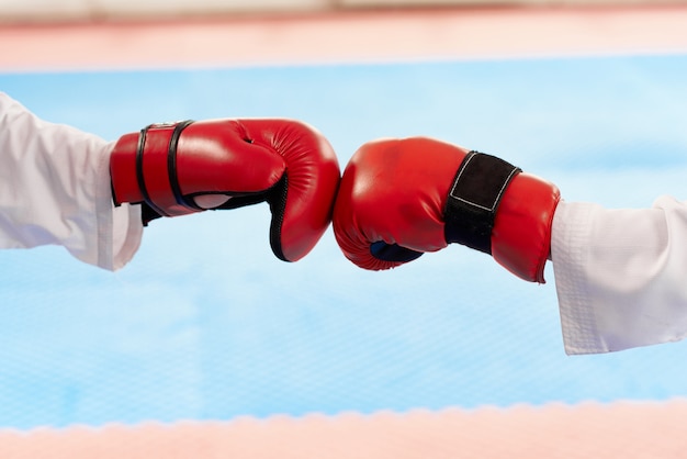 Schließen Sie oben von den roten Boxhandschuhen, die zusammen an der hellen Klasse schlagen.