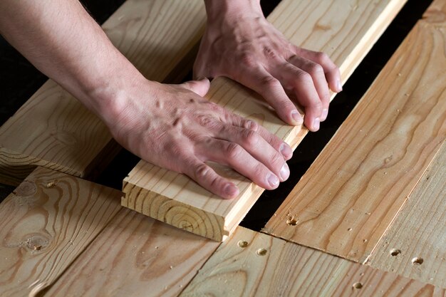 Schließen Sie oben von den starken muskulösen Händen des Berufstischlers natürliche hölzerne neue Planken auf Holzrahmenboden installierend Rekonstruktion, Verbesserung, Erneuerung und Zimmereikonzept.