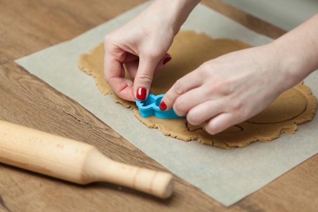 Schließen Sie oben von den weiblichen Händen, die zu Hause Plätzchen vom frischen Teig machen