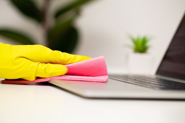 Schließen Sie oben von der Arbeiterhand, die Staub im Büro in den gelben Handschuhen abwischt