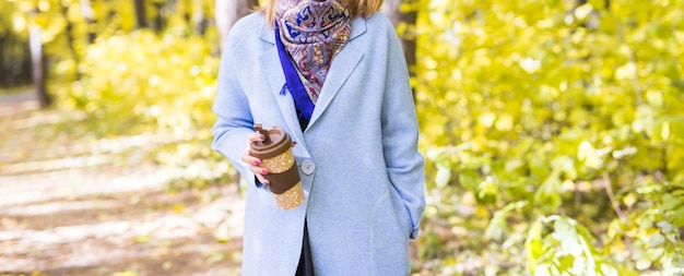 Schließen Sie oben von der Frau, die eine Tasse Kaffee zum Mitnehmen auf Herbstlandschaft hält