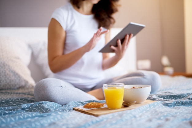 Schließen Sie oben von der Frau, die Frühstück und Saft auf Holzuntertasse hält, während Sie auf dem Bett sitzen.