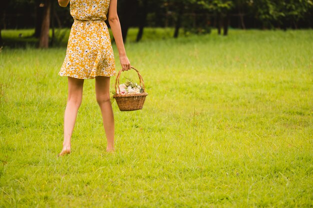 Schließen Sie oben von der Frau im gelben Kleid, das einen Korb mit Blumen hält, die auf grünes Gras gehen