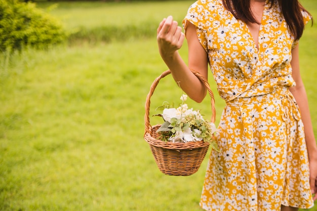 Schließen Sie oben von der Frau im gelben Kleid, das einen Korb mit den Blumen hält, die auf grünem Gras stehen