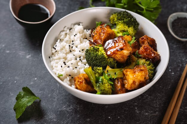 Schließen Sie oben von der gesunden Tofu-Schüssel mit Brokkoli und Reis auf schwarzem Hintergrund